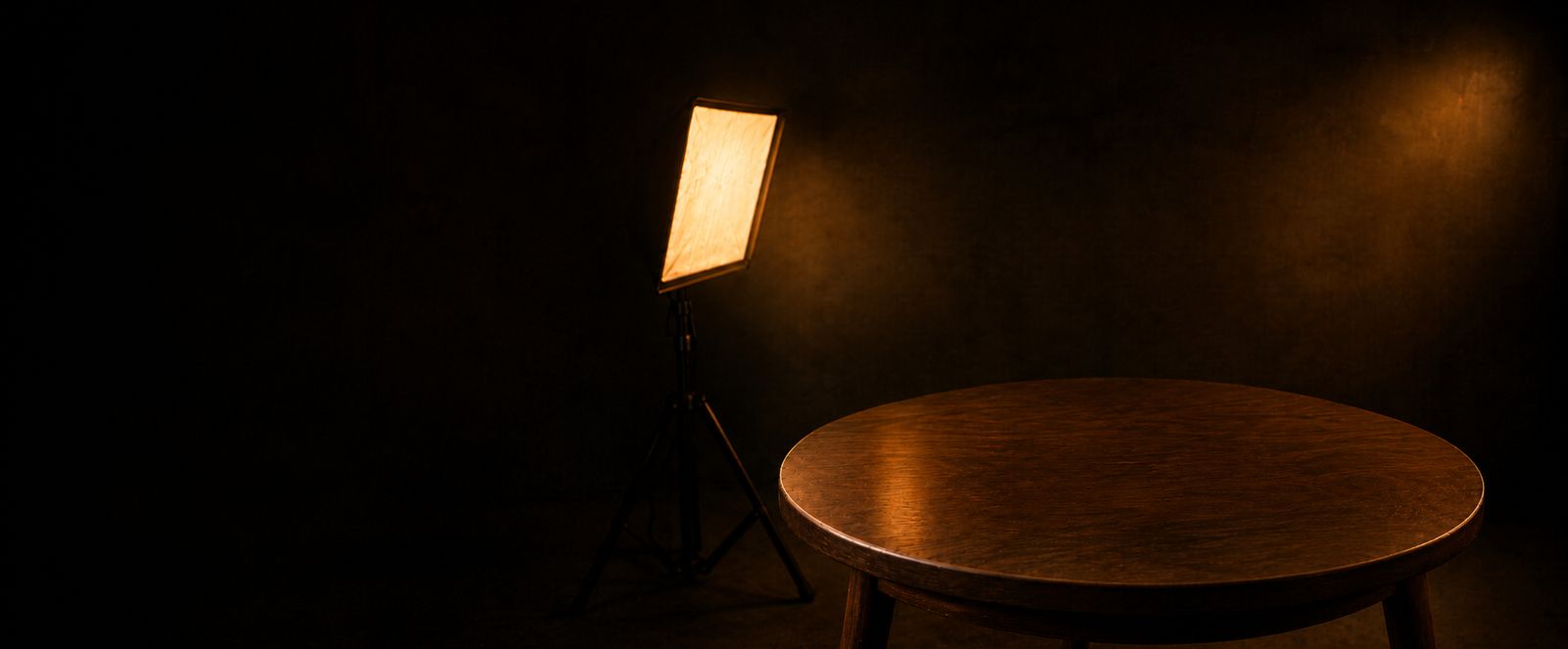 Empty studio scene: a round wooden table lit by a warm softbox against a deep warm cove background.